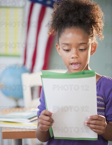 Mixed race girl reading report at school