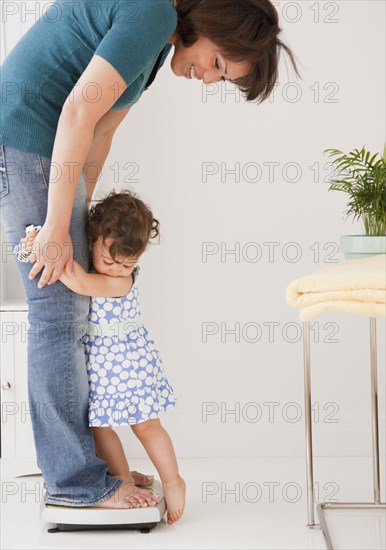 Hispanic mother weighing herself and daughter