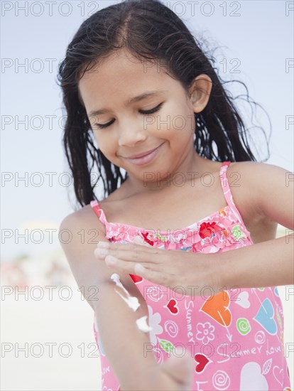 Hispanic girl applying sunscreen lotion