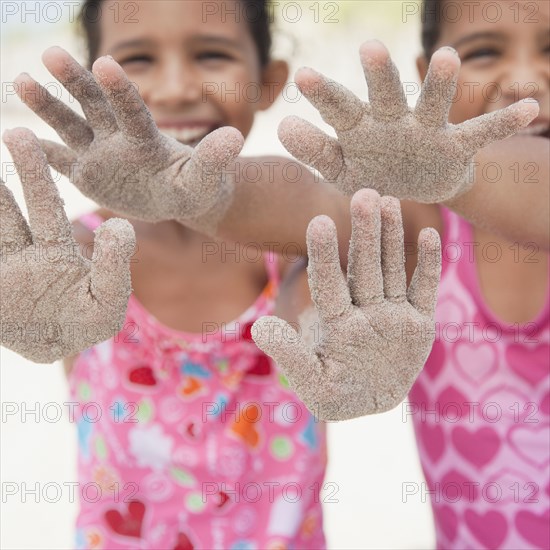 Hispanic sisters displaying sand-covered hands