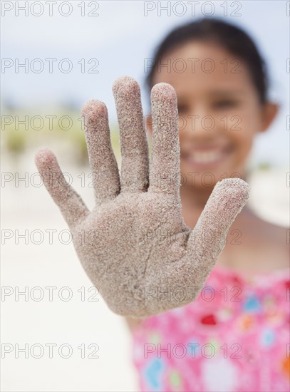 Hispanic girl displaying sand-covered hand