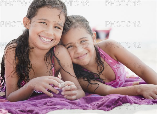 Hispanic sisters relaxing on towel at beach