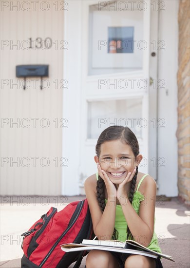 Hispanic girl sitting with school books on front stoop