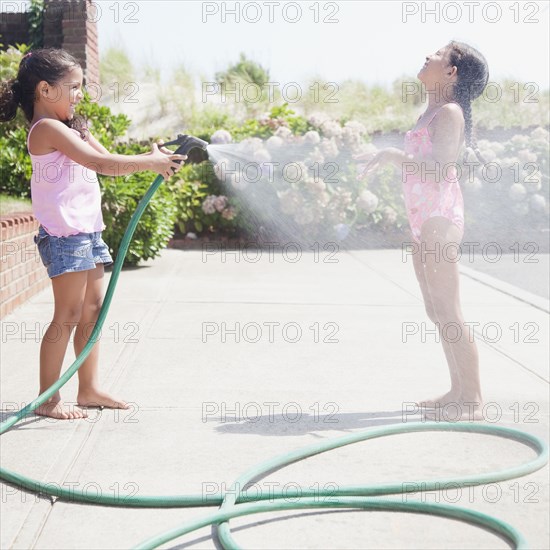 Hispanic girl spraying sister with hose