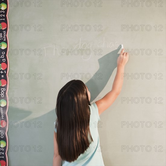 Mixed race girl writing on blackboard