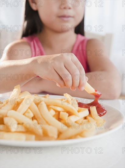 Mixed race girl eating French fries and ketchup
