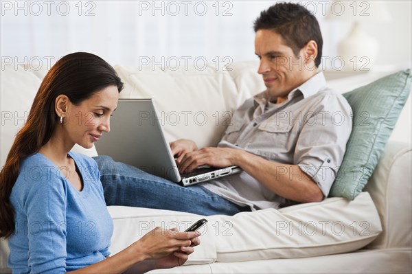 Hispanic couple with laptop and cell phone in living room