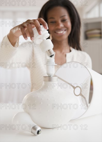 Mixed race woman putting cfl light bulb into lamp