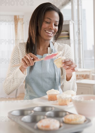Mixed race woman spreading frosting onto cupcakes