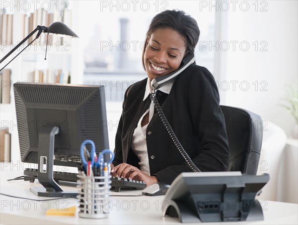 Mixed race businesswoman typing and talking on phone