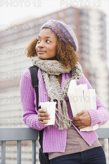 Mixed race woman holding books and drinking coffee