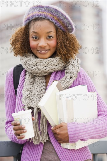 Mixed race woman holding books and drinking coffee