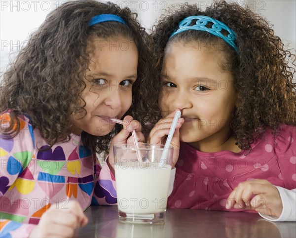 Hispanic sisters sharing glass of milk