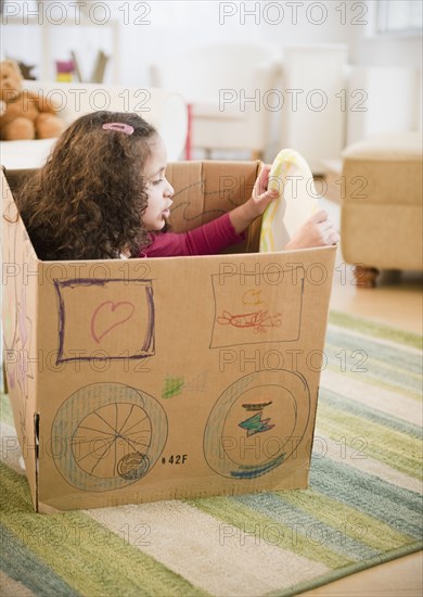 Hispanic girl playing in cardboard car