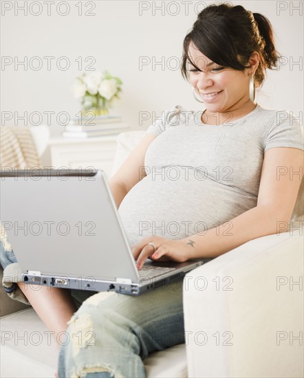 Pregnant Hispanic woman typing on laptop