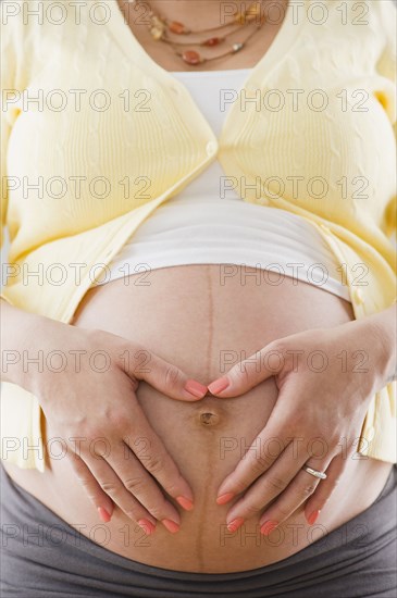 Pregnant Hispanic woman holding bare stomach