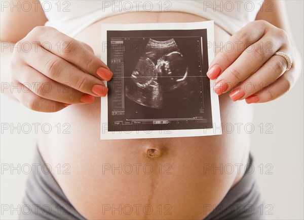 Pregnant Hispanic woman holding sonogram picture