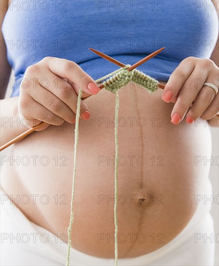 Pregnant Hispanic woman knitting with yarn