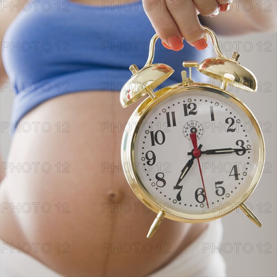 Pregnant Hispanic woman holding alarm clock