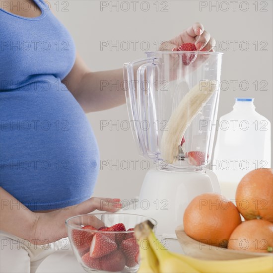 Pregnant Hispanic woman making fruit smoothie