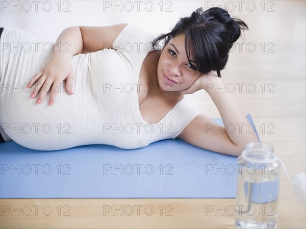 Pregnant Hispanic woman laying on yoga mat