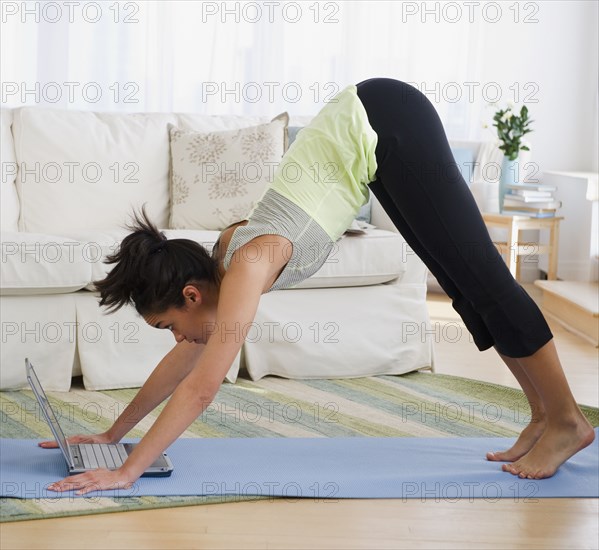 Mixed race woman practicing yoga with laptop