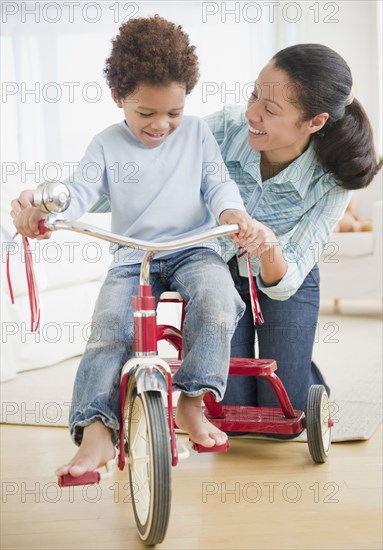 Mixed race woman teaching son to ride tricycle