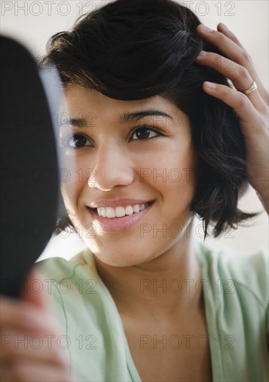 Hispanic woman looking at hair in mirror