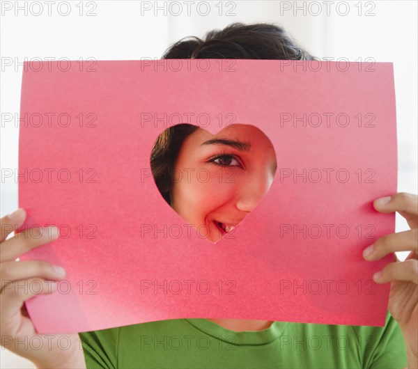 Hispanic woman looking through heart-shaped hole