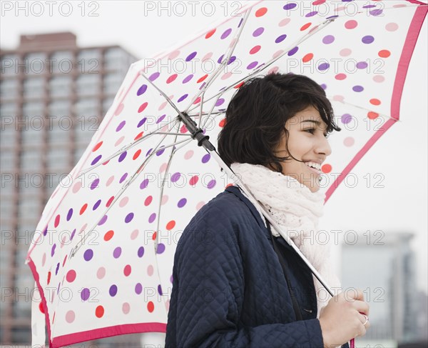 Hispanic woman walking in city with umbrella