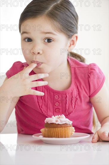 Mixed race girl licking frosting from finger