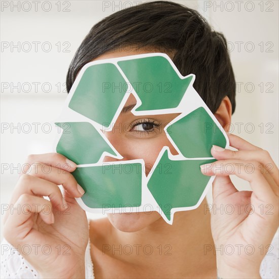 Mixed race woman holding recycling symbol in front of face