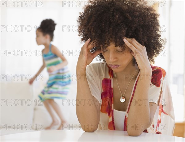 Mother with headache and daughter jumping on sofa