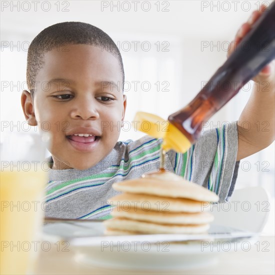 African American boy pouring syrup on pancakes