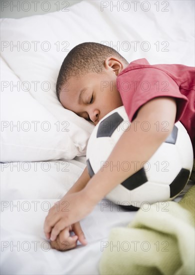 African American boy sleeping with soccer ball