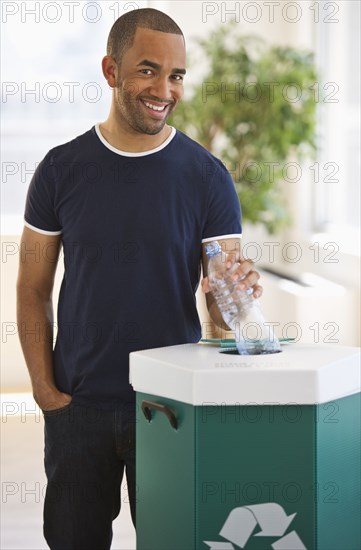 Mixed race man putting plastic bottle in recycling bin