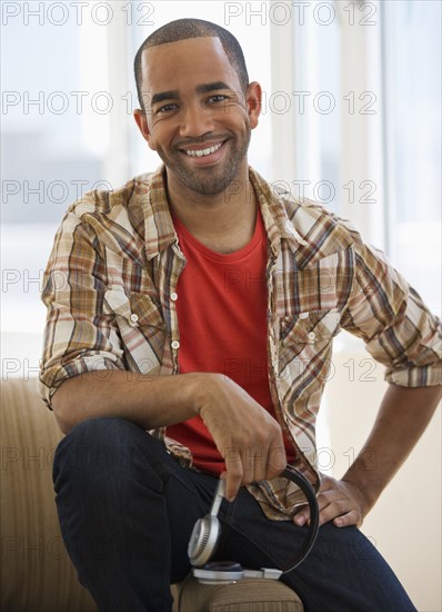 Mixed race man sitting on sofa holding headphones