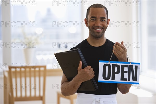 Mixed race waiter in restaurant holding menu and open sign