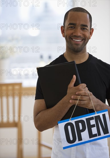 Mixed race waiter in restaurant holding menu and open sign