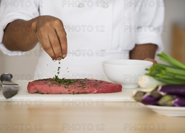 Mixed race chef seasoning steak