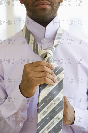 Mixed race man tying tie