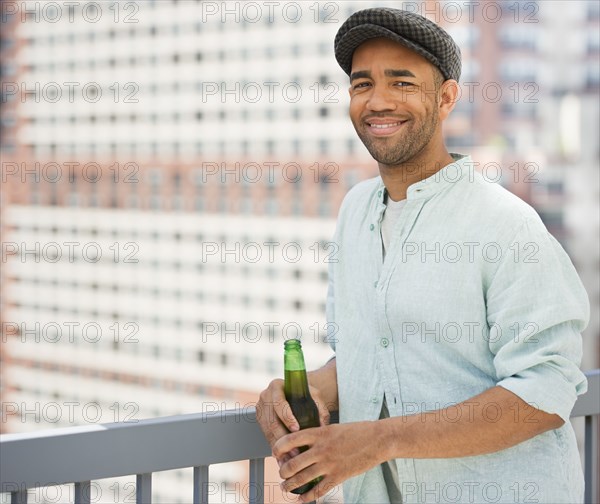 Mixed race man drinking beer near railing