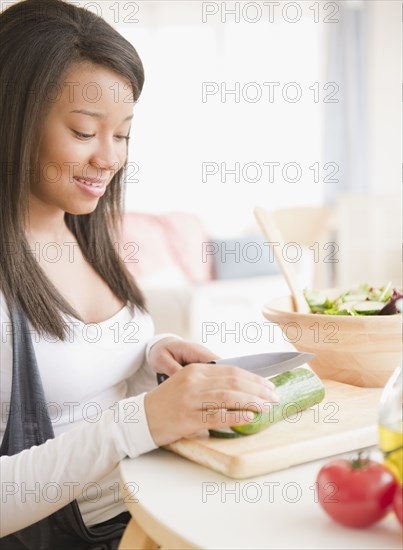 Smiling mixed race teenage girl cutting vegetables