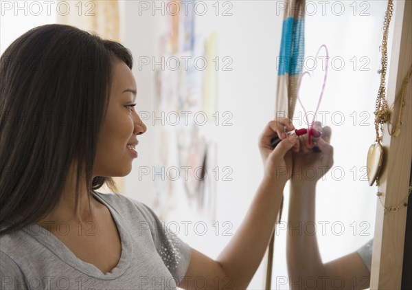 Mixed race teenage girl drawing heart on mirror with lipstick