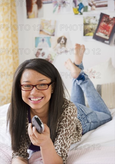 Mixed race teenage girl holding remote control and laying on bed