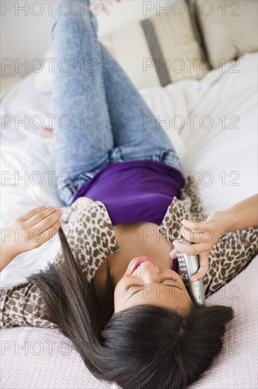 Mixed race teenage girl laying on bed and talking on telephone