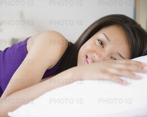 Smiling mixed race teenage girl laying on pillow