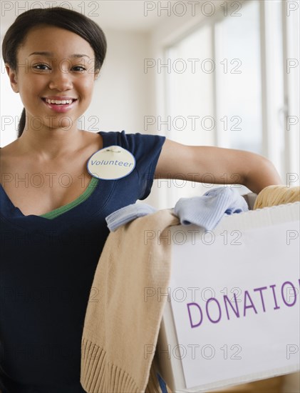 Smiling mixed race teenage girl wearing 'Volunteer' pin and holding box of donations