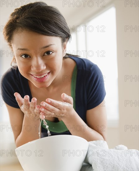 Smiling mixed race teenage girl washing face