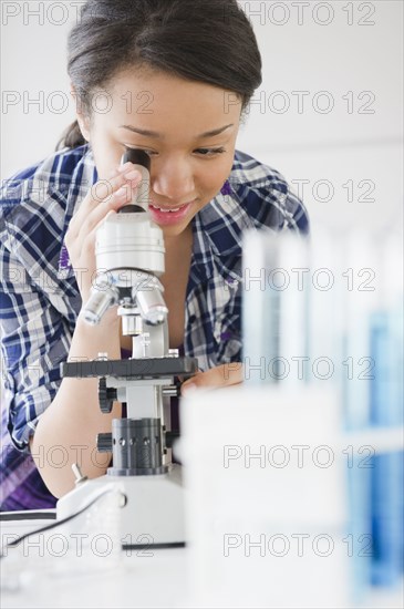 Mixed race teenage girl looking through microscope